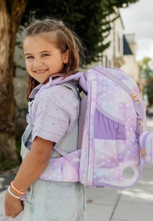 Zaino viola e lilla con un motivo a cuori, spallacci imbottiti e scomparti multipli, portato da un bambino in un abbigliamento leggero.