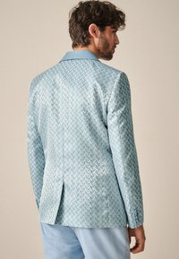 Blazer azzurro chiaro con un motivo a spina di pesce testurizzato, caratterizzato da rever a punta e uno spacco posteriore singolo. Leggero lucido e dettagli con bottoni sulle maniche.