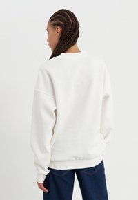 Felpa bianca leggera con spalle scese e polsini a costine, abbinata a jeans larghi blu scuro. Design semplice e rilassato.