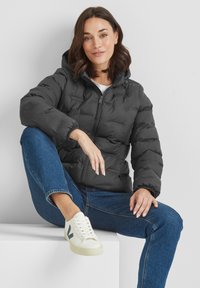 Black puffer jacket with a hood, quilted design, elastic cuffs, and front zipper. Paired with blue denim and white sneakers.