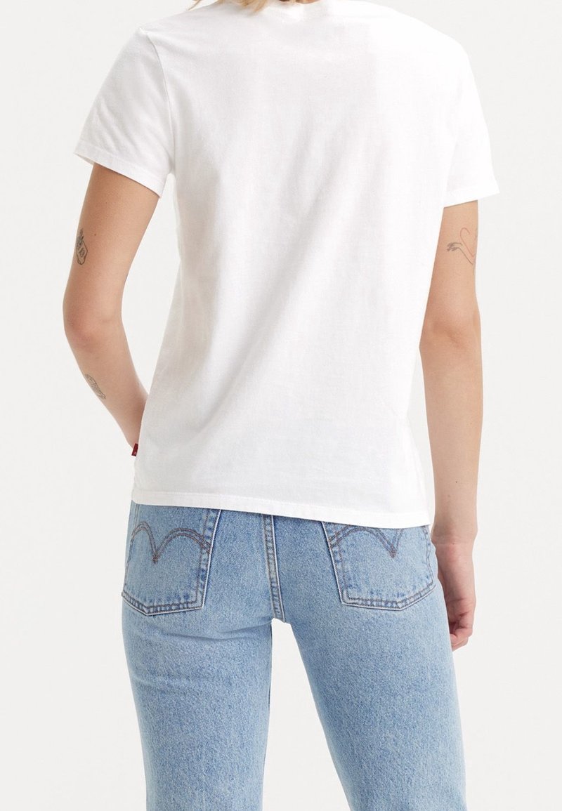 T-shirt blanc à manches courtes en coton, avec une coupe droite et une texture douce, associé à un jean taille haute bleu clair avec des accents de couture.