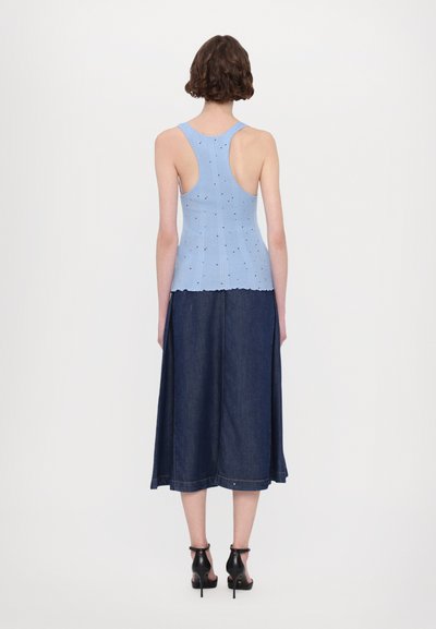 Lyseblå, ribbestrikket smal skjorte med bølget kant, sammen med en lang, mørk denimskjørt. Modellen har på seg svarte sandaler med stropper.
