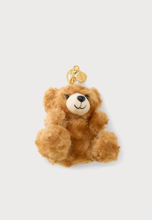 Lille brun fluffy bamse-nøglering med smilende ansigt og guldlukning, fastgjort på en hvid baggrund.