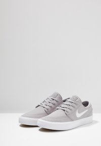 Graue Leinensneaker mit einem weißen Logo, runder Zehenpartie, flacher Sohle und klassischem Schnürdesign mit genähten Details.