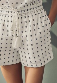 Vita shorts i lättviktig tyg med marinblå broderade mönster. Elastisk midja med dragsko och detaljer i tofs.