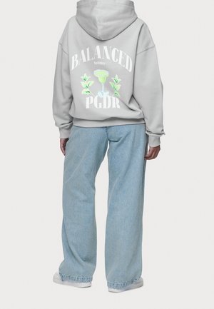 Henkilö, jolla on harmaa huppari, jossa takana teksti "BALANCED summer PGDR" sekä vihreän cocktaillasin ja lehtien kuva, yhdistettynä väljiin sinisiin farkkuihin.