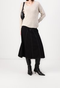 Svart A-linjeformad kjol med kontrasterande vit sömnad, kombinerad med en beige tröja och knähöga svarta läderstövlar. Axelremsväska ingår.