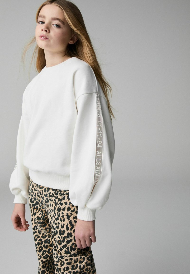 Vit sweatshirt med ribbade muddar och texten "ALLSAINT'S 01-11-94" på ärmen, matchad med leopardmönstrade byxor.