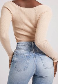 Haut ajusté beige à rayures avec des manches longues, associé à un jean en denim léger bleu clair taille haute, mettant en valeur des poches arrière et une texture légèrement déteinte.