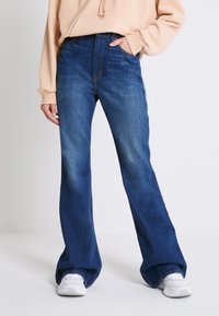 Jeans svasati blu scuro in tessuto denim con una texture leggermente sbiadita. Design a vita alta con cuciture visibili e una vestibilità casual.