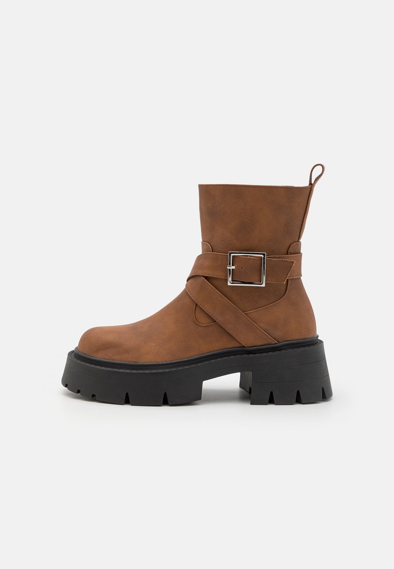 Brown faux leather ankle boot with a chunky black platform sole. Features a side buckle strap and a pull tab at the back.
