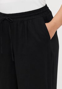 Pantalons noirs à taille élastique avec cordon de serrage, dotés de poches latérales et d'une texture douce et lisse.