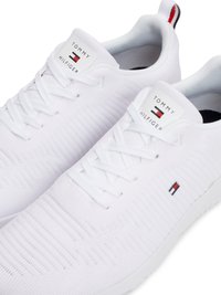 Scarpe da ginnastica bianche con tomaia in mesh testurizzato, dotate di chiusura con lacci e linguetta con logo. Include iconici dettagli in rosso, bianco e blu.