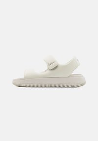Valkoiset Nike-sandaalit, joissa on sileä synteettinen yläosa, kaksi säädettävää hihnaa, pehmustettu pohja ja kuviollinen ulkopohja, joka tarjoaa pidon.