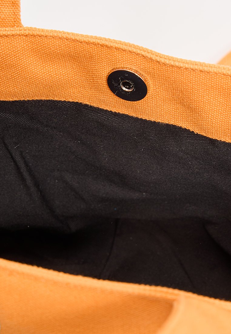 Bolsa de lona con exterior naranja y interior de tela negra, que cuenta con un cierre a presión metálico y bordes estructurados.