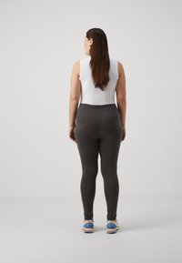 Dark gray leggings with a stretchy, fitted design, featuring a smooth texture and an elastic waistband, paired with colorful athletic shoes.