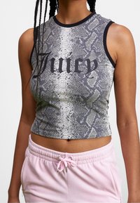 Femme portant un crop top gris sans manches à motif serpent avec le texte noir "Juicy" et un pantalon rose clair à cordon.