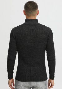 Svart ribbestrikket turtleneck genser med et teksturert mønster, tettsittende form og lange ermer. Materialet ser mykt og varmt ut.
