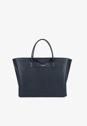 Sac fourre-tout en cuir bleu marine avec une forme structurée, deux poignées supérieures, et un accent en rabat portant un logo. Surface texturée avec un design minimaliste.