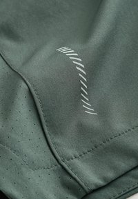 Gros plan sur un tissu gris-vert avec des coutures cousues, de petits trous de ventilation et un motif de bande courbe réfléchissante.