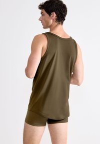 Olivově zelený bezrukávový top vyrobený z hladké látky, doplněný o odpovídající fitted kraťasy. Jednoduchý design s minimálními akcenty.