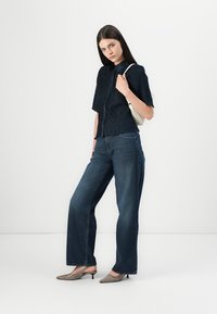 Marineblauwe cropped korte mouwen shirt met een gestructureerde afwerking, gecombineerd met wijde, donkere denim jeans en grijze puntige hoge hakken.