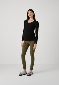 Camiseta negra de manga larga con escote de encaje, pantalones ajustados verde oliva y sandalias celestes con tiras ajustables y detalles estampados.