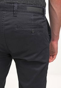 Marineblaue Baumwollhosen mit glatter Textur, ausgestattet mit einer knöpfbaren Gesäßtasche und einem kleinen Logo-Patch am Bund.