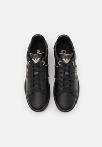 Black leather sneakers with round toe, gold accents, flat laces, and "EA" logo. Textured surface and contrasting stitching details.