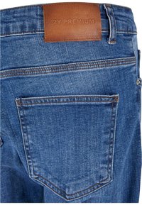 Jeans de mezclilla azul con un acabado texturizado, presentan un parche de cuero marrón en la cintura y un bolsillo trasero con costuras en contraste.