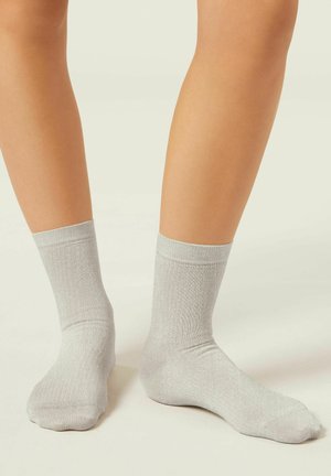Graue Socken aus metallischem Stoff mit einer gerippten Struktur und einem Knöchellänge-Design. Die Farbe wirkt leicht reflektierend.