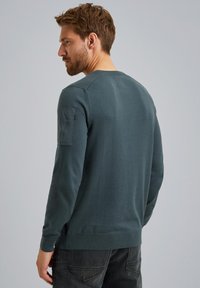 Dunkelgrüner Langarmpullover, strukturiertes Material, gerippter Rundhalsausschnitt und Rippbündchen, mit einer Utility-Tasche am linken Ärmel, lässige Passform.
