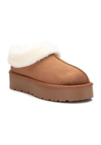 Zapatilla de ante marrón con un cuello de piel sintética blanca, que cuenta con una suela gruesa y texturizada y una forma redondeada, diseñada para la comodidad y el calor.