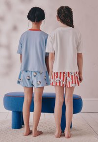 Deux enfants se tiennent dos à dos, portant un t-shirt bleu avec des accents rouges et un t-shirt blanc. Le short bleu présente un motif Hello Kitty ; le short rayé rouge affiche des personnages de dessin animé.