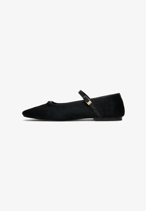 Schwarze spitze Mary Jane flache Schuhe mit einem dünnen verstellbaren Riemen und goldener Schnalle auf einem weißen Hintergrund.
