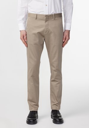 Beige Chinos aus Baumwolle mit geradem Bein. Sie verfügen über einen Gurtbandbund und seitliche Taschen, kombiniert mit schwarzen Schuhen.