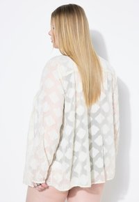 Lettet, gennemsigtig blouse i creme med et struktureret mønster. Har lange ærmer, en afslappet pasform og et let gennemsigtigt stof.