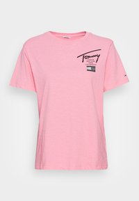 Różowa bawełniana koszulka z okrągłym dekoltem, krótkimi rękawami i czarnym nadrukowanym logo z nazwami miast na przodzie. Gładka tekstura.