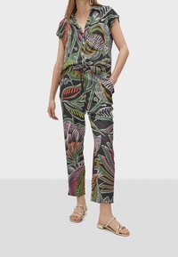 Set di camicia con bottoni e pantaloni in verde scuro con motivi astratti di foglie colorate. Include tasche e vita con cordoncino. Sandali con laccetti.