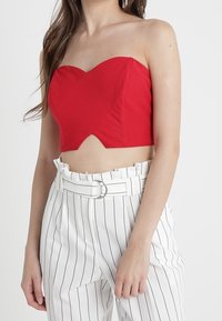 Kvinna i en strapless röd crop top och högmidjade vita byxor med svarta vertikala ränder samt ett bälte med en metallring.