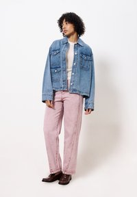 Denimjack met twee borstzakken, lichtblauwe kleur, ontspannen pasvorm. Draagt bij lichtroze hoge taillebroek en donkerbruine instappers.