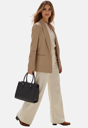 Blazer beige, blouse bianca, pantaloni crema e borsa a tracolla trapuntata nera. Modella tiene la borsa con manici neri, indossando stivaletti con tacco marroni.