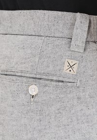 Jasnoszare spodnie teksturowane z subtelnym wzorem w kropki, z przednią kieszenią, małą metką i białym guzikiem jako detalem.