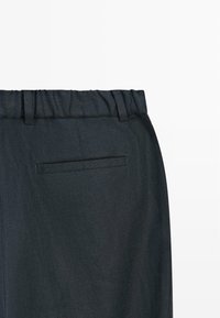 Pantalon gris foncé avec une taille élastique et une seule poche passepoilée à l'arrière, présenté sur un fond blanc.