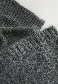 Graue Strickstoffabschnitte, einer mit vertikaler Rippung und der andere mit einer flauschigen, strukturierten Oberfläche. Beide zeigen verschiedene Grautöne.
