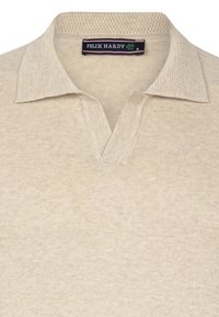 Camisa de polo de punto color beige con un cuello texturizado y un pequeño escote en forma de V. Presenta una etiqueta de marca etiquetada "FELIX HARDY" dentro del cuello.