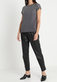 Šedá košile s krátkým rukávem, na horní části zdobená gradientem stříbrných hrotů; kombinovaná s černými koženými kalhotami a černými muly na blokovém podpatku.