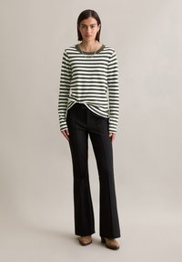 Green and white striped long-sleeve shirt paired with black flared pants. The model stands on a neutral backdrop, featuring a simple design.