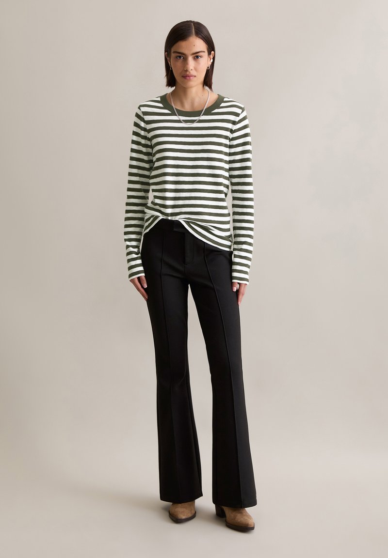 Camicia a maniche lunghe a righe verdi e bianche abbinata a pantaloni neri svasati. Il modello si trova su uno sfondo neutro, con un design semplice.