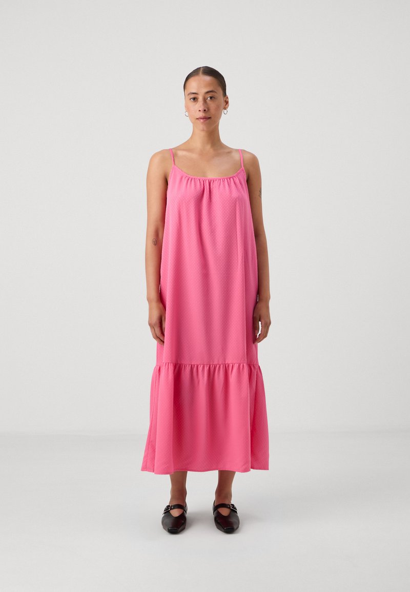 Ροζ αμάνικο μαξι φόρεμα με συγκεντρωμένο ντεκολτέ, υφασμάτινο μοτίβο με πουά και ραφή με φρου-φρου στο στρίφωμα, συνδυασμένο με μαύρα παπούτσια.